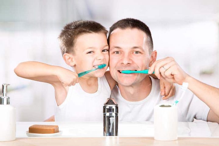 smiling child brushes his teeth with dad in the bathroom