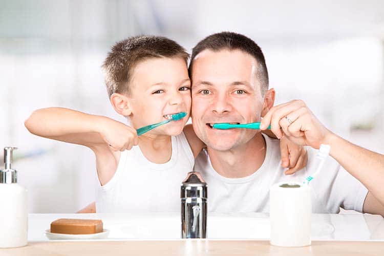 smiling child brushes his teeth with dad in the bathroom