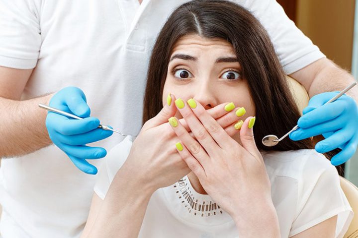 Hate checkups! Shot of a young scared woman covering her mouth with her hands being scared of the dental examination